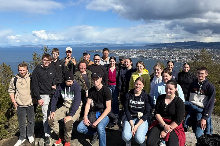 Group of people on a rocky hilltop with a sea view in the background under a blue sky.