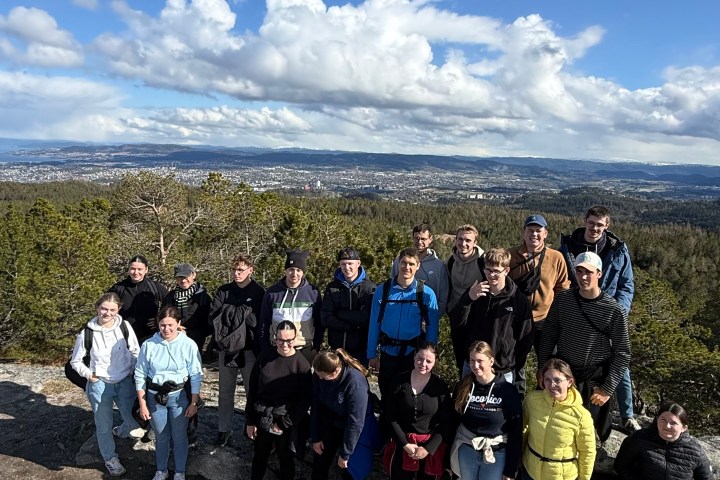 Group of people posing on rocky terrain with a scenic mountain view under a blue sky.
