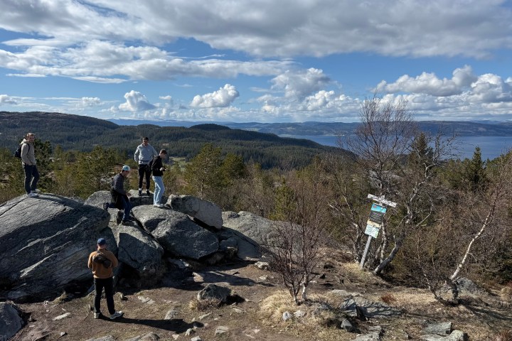 Hikers on rocky terrain overlooking a forested landscape and lake under a cloudy sky.