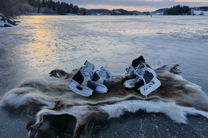 Ice skates on fur rug on frozen lake at sunset, with distant trees and hills.