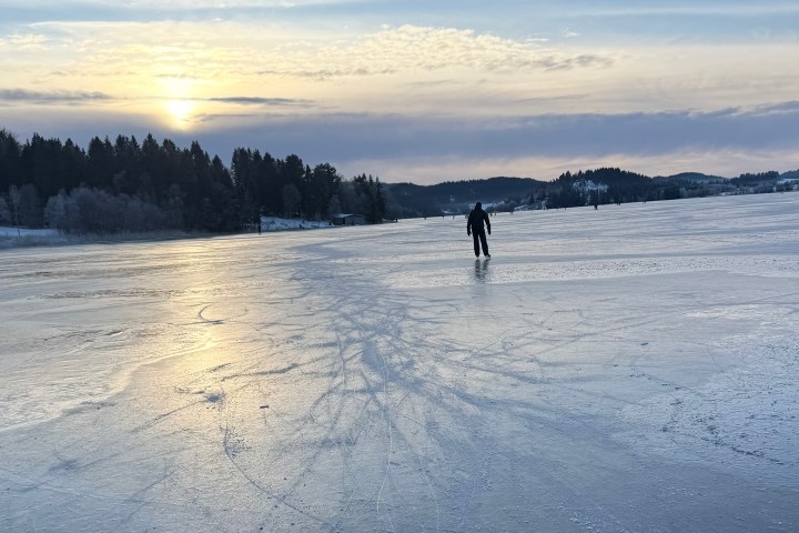 Person ice skating on a frozen lake and sunset in the background.