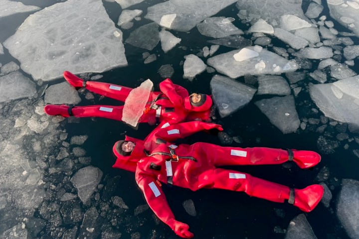 Two people in red suits floating among ice in cold water.