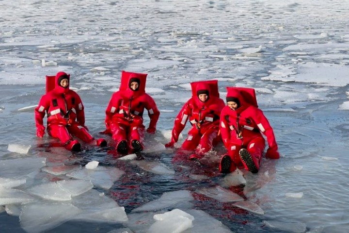 Four people in red survival suits sitting on ice-covered water.