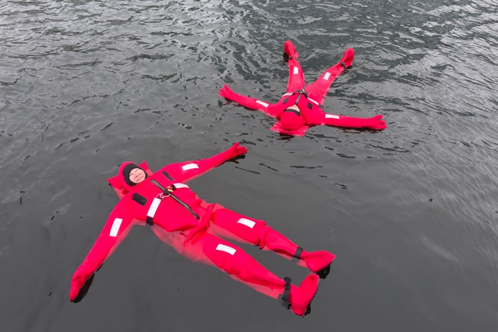Two people in red survival suits floating on water.