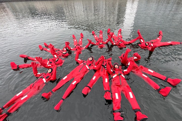 People in red suits floating on water with arms raised.