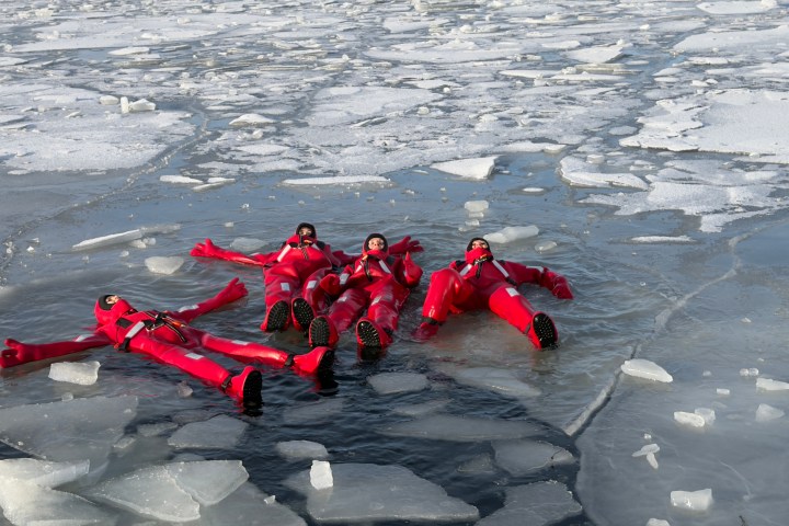 Four people in red survival suits floating on ice-covered water.