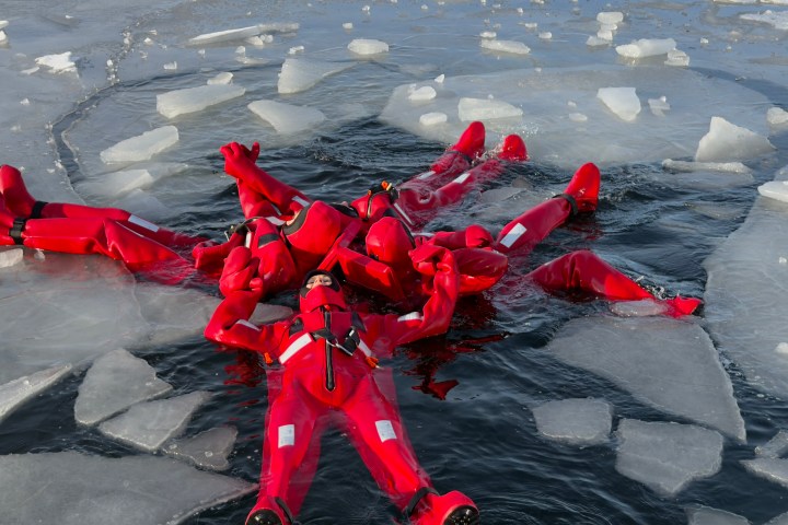 Group in red suits floating on icy water surrounded by broken ice.