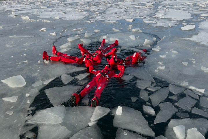Five people in red suits form a star shape on icy water surrounded by ice.