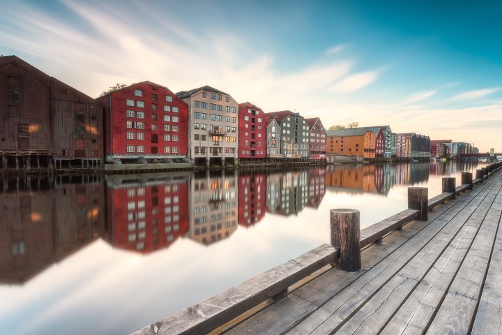 Colorful wooden buildings reflecting in a calm river, with a wooden walkway in the foreground.