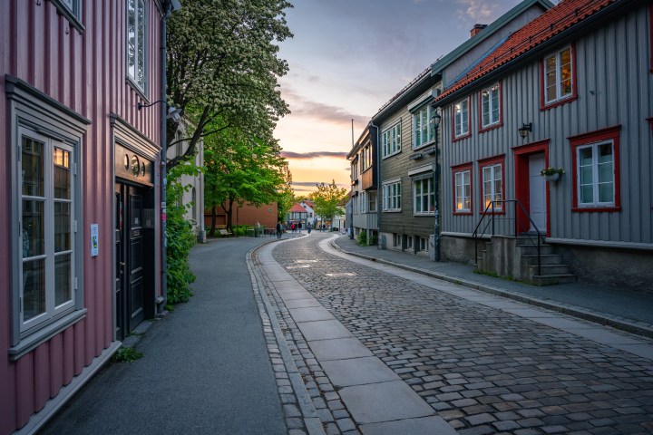 Curved cobblestone street with colorful wooden houses at sunset.