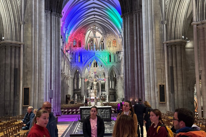 People inside a cathedral with colorful lights on arches.