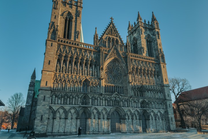 Gothic cathedral facade with intricate sculptures and large rose window under clear blue sky.